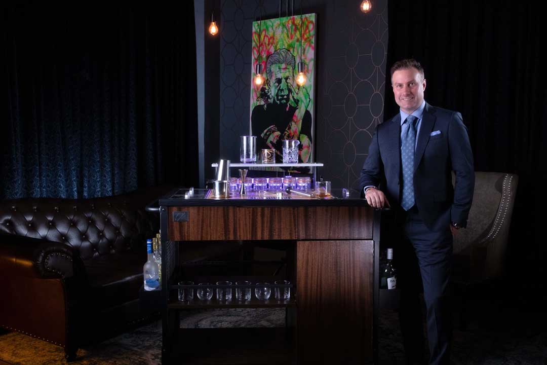 Chris Adams leaning on the Rustica Mixology Cart in a chic meeting room